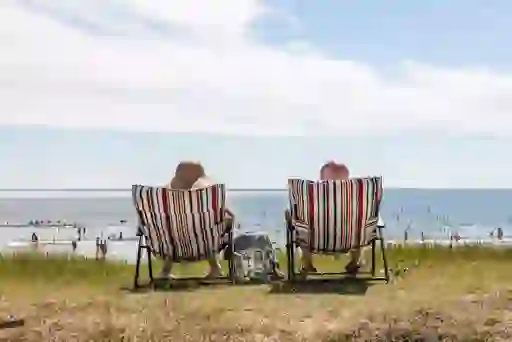 Two people relaxing on striped deck chairs overlooking a busy beach on a sunny summer day in Youghal, County Cork.