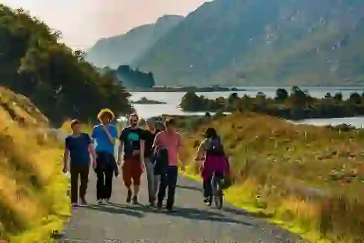 Group of people walking and cycling on a lakeside trail in Glenveagh National Park, Donegal, with mountains behind.