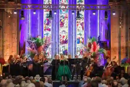 Orchestra performing at Kilkenny Arts Festival inside a cathedral with stained glass windows and vibrant floral decor.