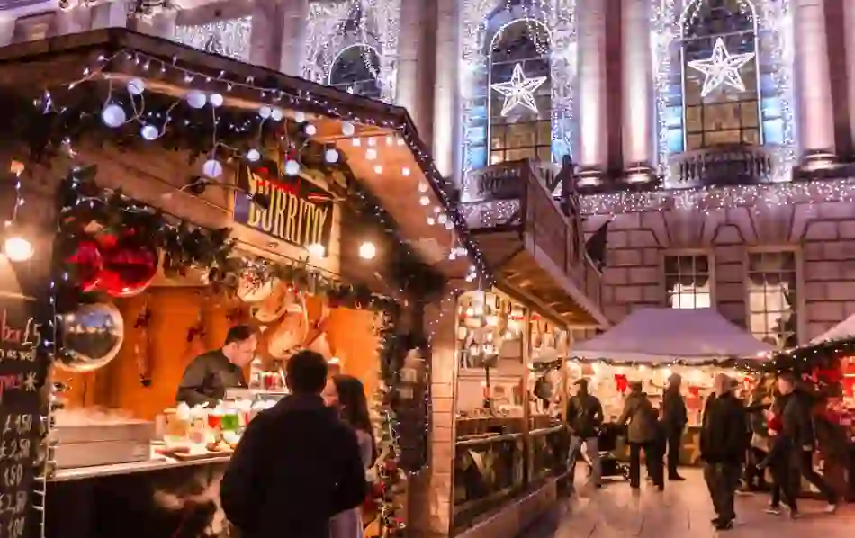 People browsing food and gift stalls at a Christmas market with bright decorations in Belfast.