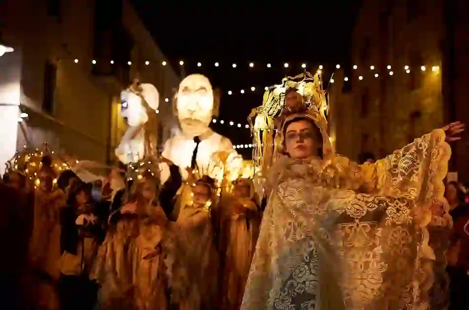 Performer in ornate lace costume with glowing headpiece leads night-time Halloween parade with giant lantern puppets in Limerick.
