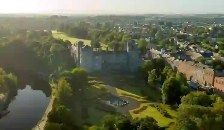 Aerial view of Kilkenny Castle and landscaped gardens beside the River Nore, with morning light over the city and surrounding countryside.