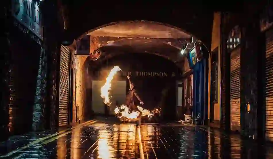 Fire performer spins flaming props in an arched alleyway at night, with wet cobblestones reflecting the glow in Limerick.