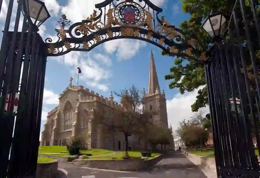 St Columb’s Cathedral in Derry~Londonderry, viewed through ornate iron gates with a tall spire and stone walls.