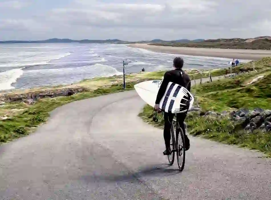 Surfer cycling with board towards Bundoran Beach in County Donegal on a cloudy day.
