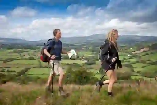 Two hikers with walking poles cross a grassy hill overlooking rolling countryside in the Wicklow Mountains.