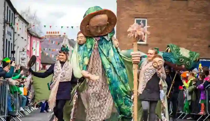Giant green-cloaked figure leads St Patrick’s Day parade through Kilkenny streets lined with spectators.