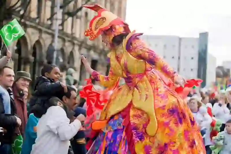 Performer in vibrant costume high-fives a child during Belfast’s St Patrick’s Day parade.