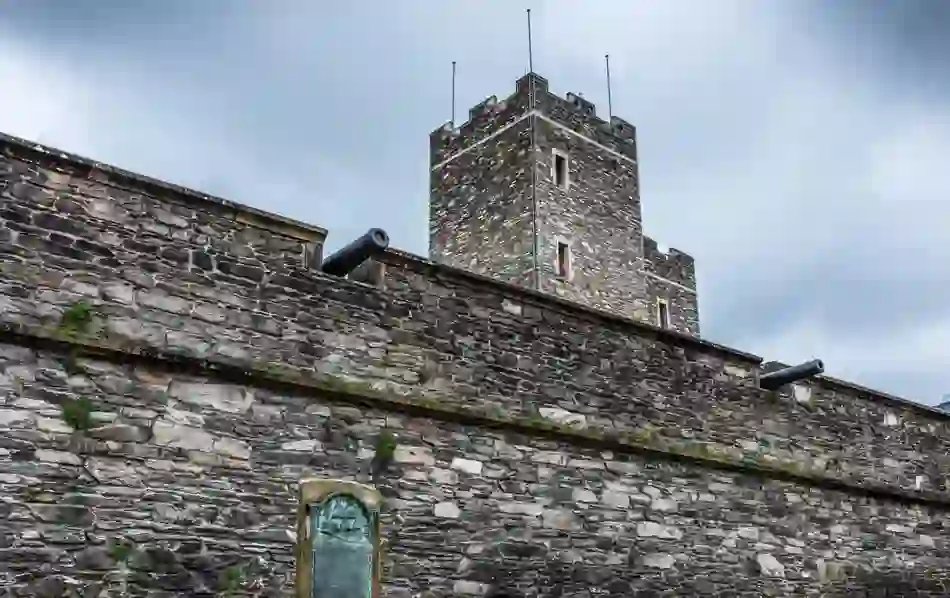 Stone walls and tower of Derry~Londonderry with cannons on display against a cloudy sky.