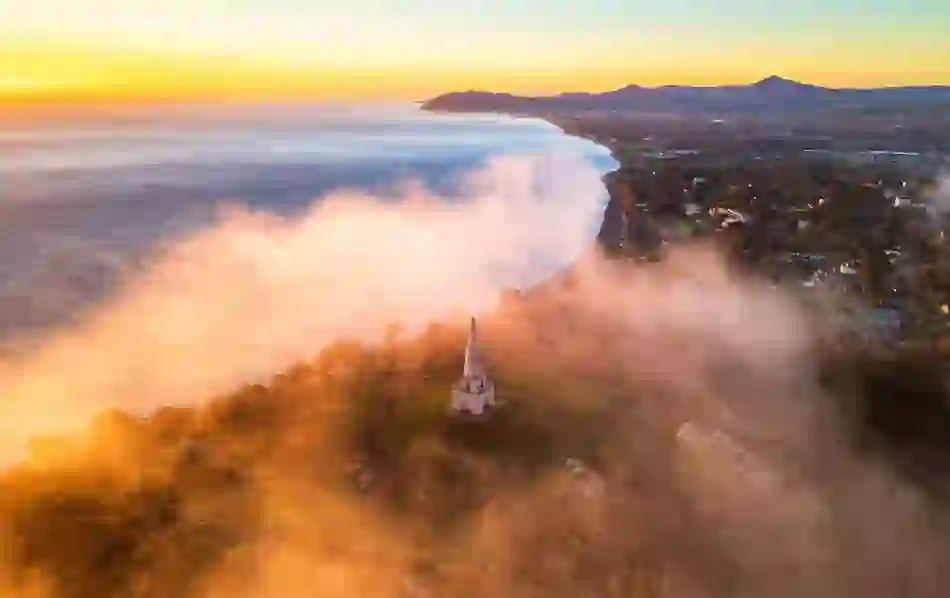 A white obelisk stands above low-lying mist on Killiney Hill at sunrise.