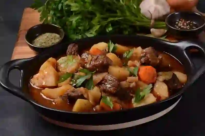 Hearty Irish beef and Guinness stew with potatoes, carrots and fresh parsley in a cast-iron dish.