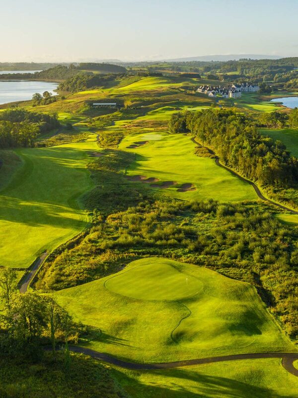 Scenic aerial view of Lough Erne Golf Resort with green fairways, lakes, and surrounding hills at sunset.