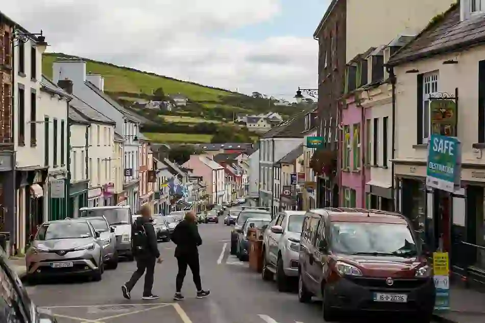 Busy main street in Dingle, County Kerry, with cars parked and people walking past colourful buildings.
