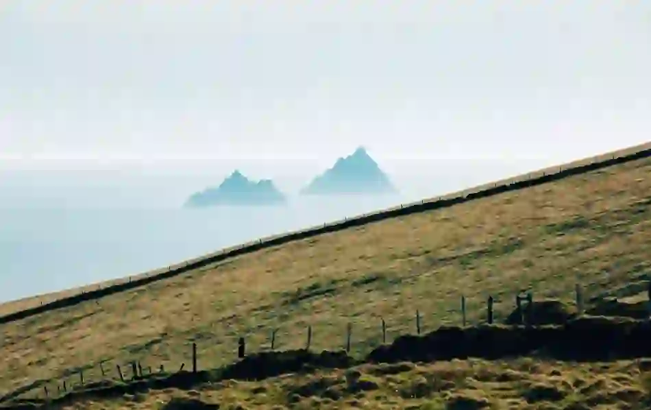 The Skellig Islands rise from the Atlantic, viewed from rolling green hills along the County Kerry coastline.