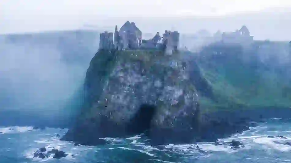 Ruined Dunluce Castle above the Atlantic Ocean in misty weather on the County Antrim coast.