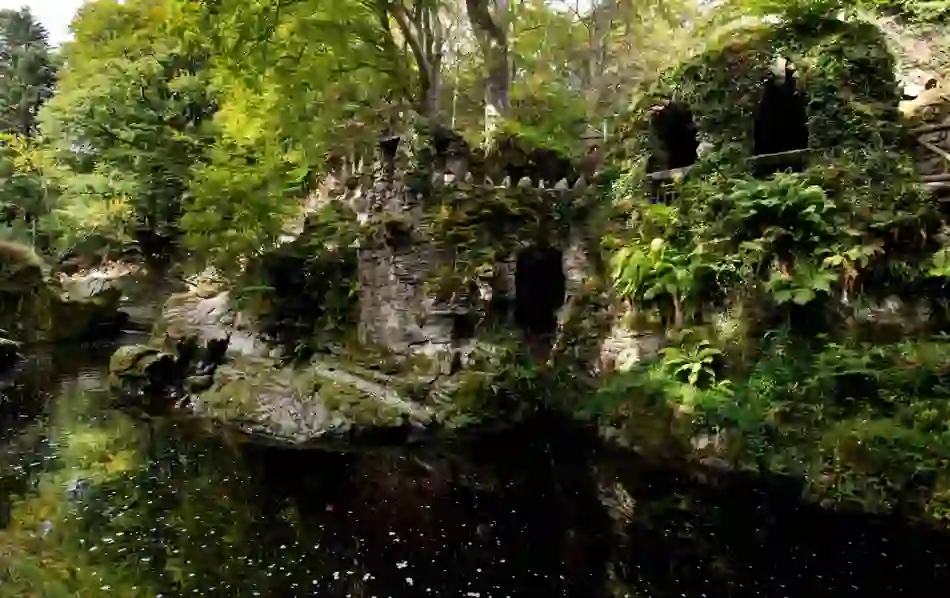 Ancient-looking stone grotto covered in moss and ferns beside a still stream in the Mourne Mountains, County Down.