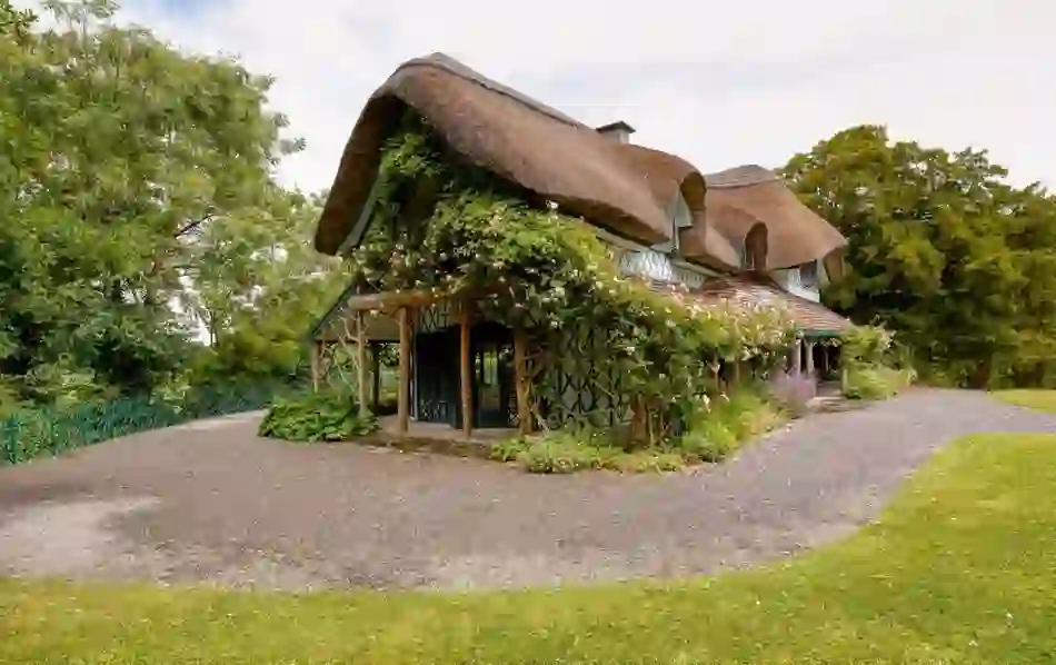 Ornate thatched Swiss Cottage with timber detail, flowers and roses, set in lush gardens in County Tipperary.