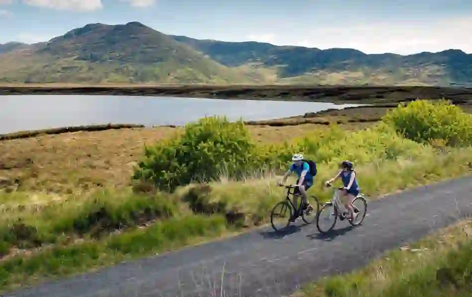 Two cyclists riding along the Great Western Greenway with mountains and a lake in the background, County Mayo.