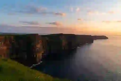 Sunset at Cliffs of Moher, County Clare, with warm light over dramatic sea cliffs and Atlantic Ocean.