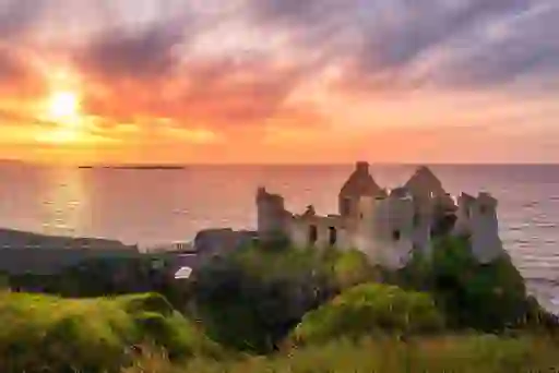 Sunset over Dunluce Castle ruins, County Antrim, with golden sky reflecting on the Atlantic waves.
