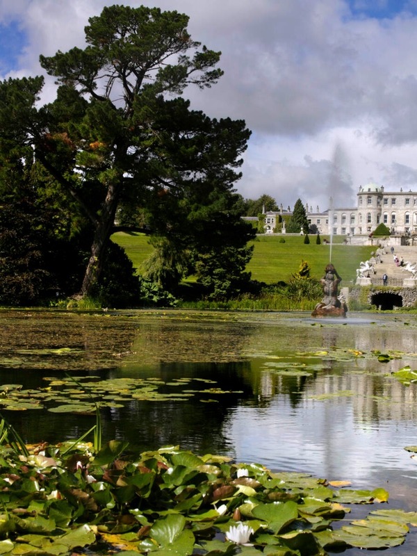 Powerscourt Gardens lake view with fountain, statues, and the grand estate in the background.