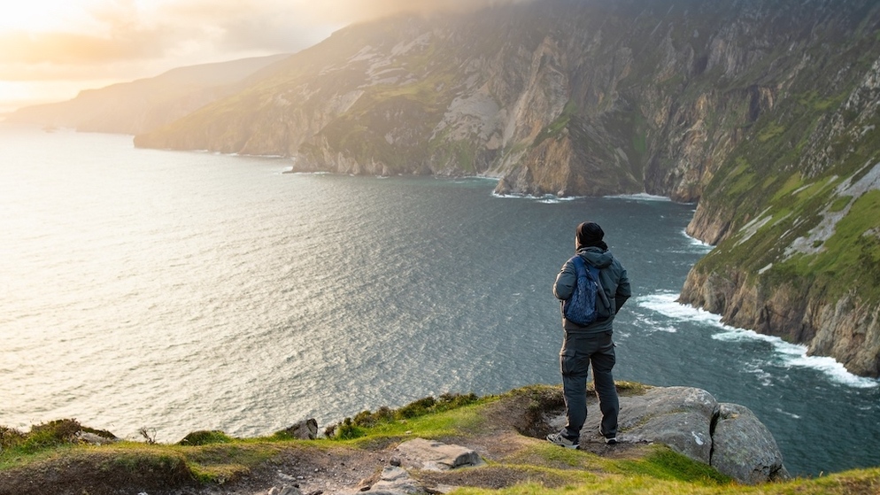 Hiker standing on a cliff edge overlooking the dramatic coastline at Slieve League, County Donegal.