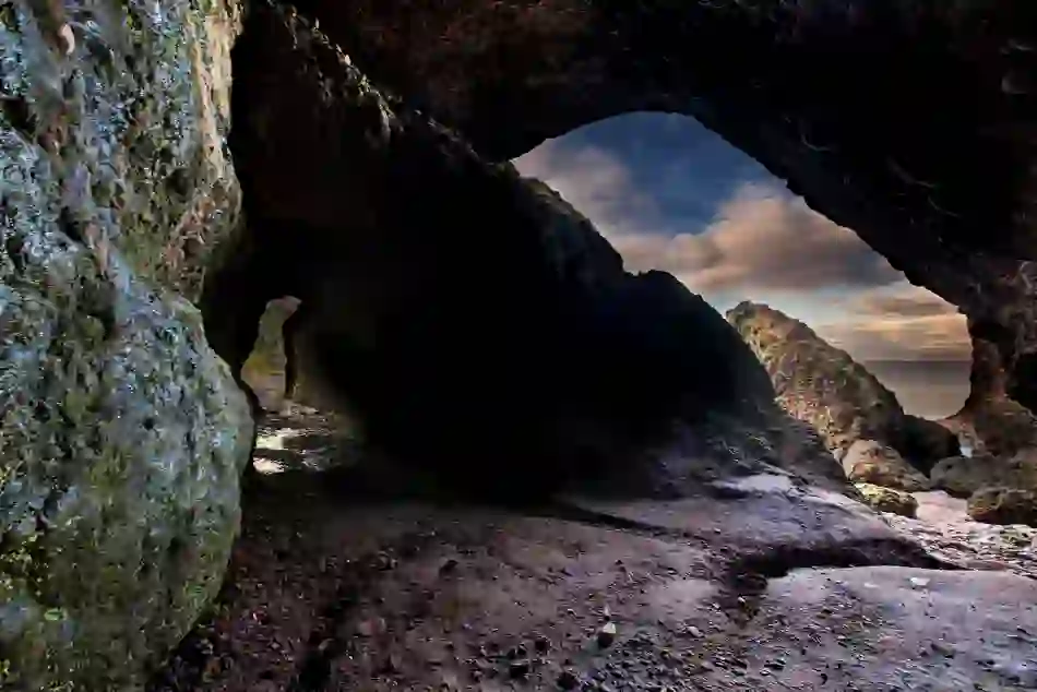 Dark, rocky Cushendun Caves opening to a coastal view under a blue sky in County Antrim, Northern Ireland.