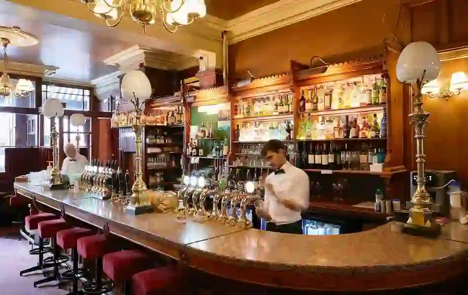 Bartender at Neary’s pub in Dublin prepares drinks behind a polished bar with brass taps and red velvet stools.