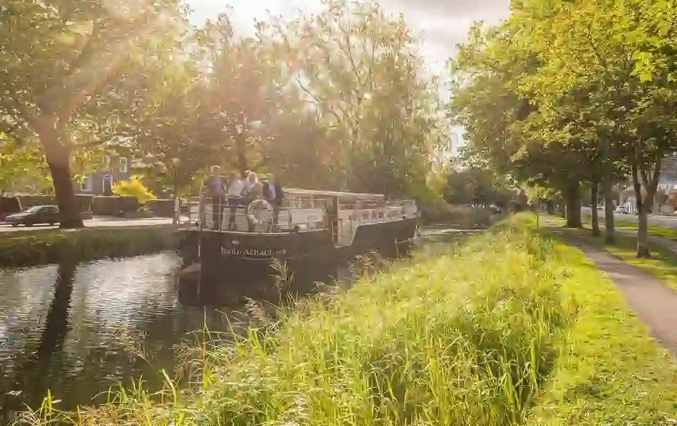 Group of people enjoying a sunny cruise aboard a canal barge on Dublin’s leafy Grand Canal near Portobello.