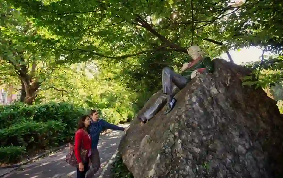 Visitors admire the colourful Oscar Wilde statue lounging on a rock in leafy Merrion Square Park, Dublin.