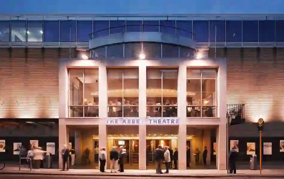 Evening view of Dublin’s Abbey Theatre with warmly lit windows and theatre-goers gathered outside before a show.