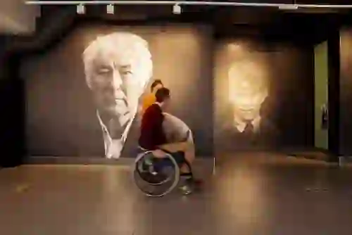 Person in a wheelchair passing portraits of poet Seamus Heaney as adult and child at Seamus Heaney HomePlace, Bellaghy.