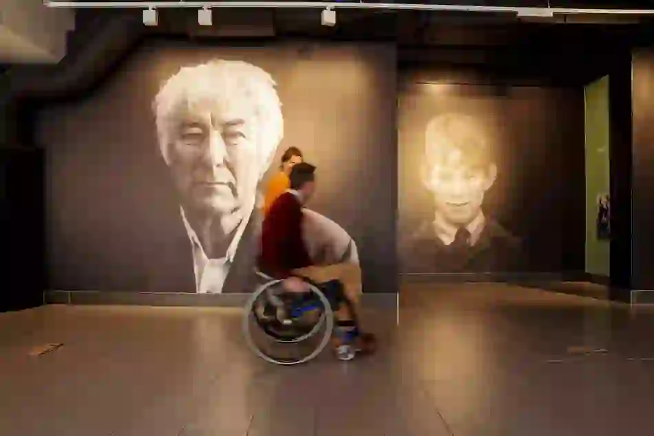 Portraits of Seamus Heaney and his younger self at HomePlace; visitors pass by, immersed in his story.