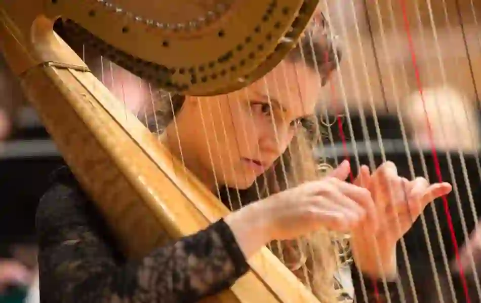 Harpist performs at Sixes and Sevens concert, her face framed by strings as she plays with focus.