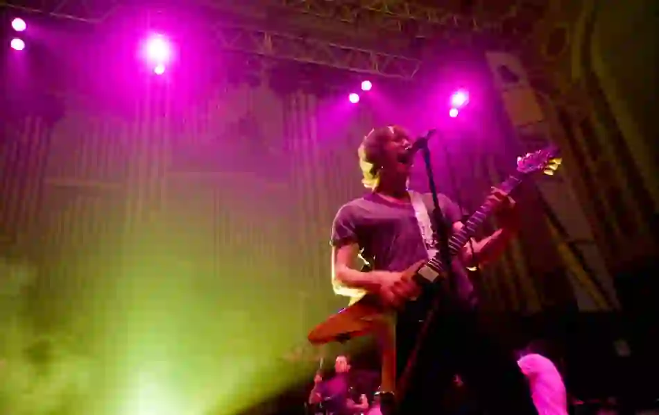 Rock musician singing and playing electric guitar under purple and yellow stage lights at Belfast’s historic Ulster Hall.
