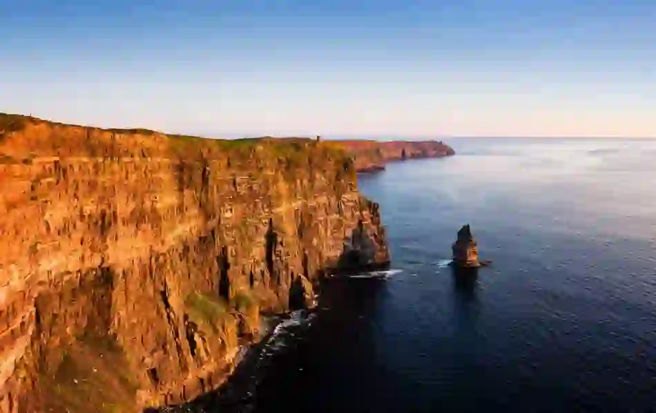 Sunset at the Cliffs of Moher, Clare, with sea stacks and rugged coastline lit by golden Atlantic light.