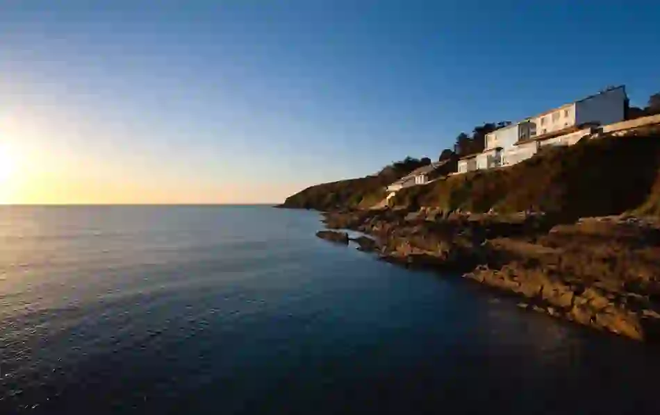 Cliff House Hotel overlooking Ardmore Bay, Waterford, lit by golden sun with rocky coast and calm sea below.