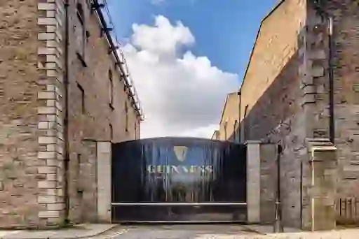 Guinness Storehouse gate at St James’s Gate in Dublin, framed by historic stone buildings and blue skies above.