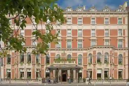 Grand facade of The Shelbourne Hotel on St Stephen’s Green, Dublin, with Irish flag and passers-by at entrance.