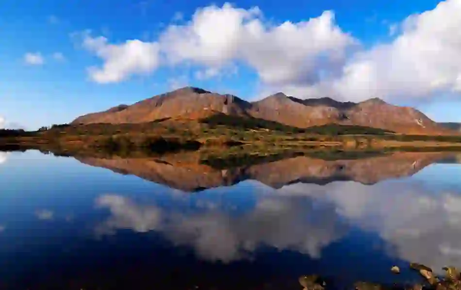 Cloud-covered Twelve Bens mountains mirrored in the calm waters of Lough Inagh in Connemara.
