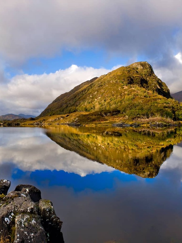 Sunlit mountain reflected in still waters at the Lakes of Killarney near the Gap of Dunloe, County Kerry.