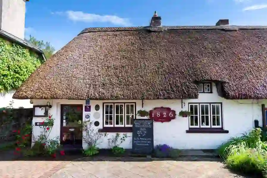 Thatched cottage housing the 1826 Adare Restaurant with white façade, flowers, and a chalkboard menu outside.