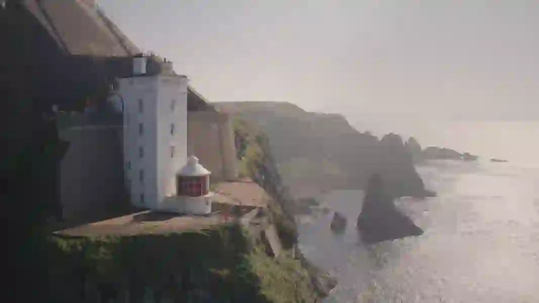 White lighthouse perched on a cliff edge at Rathlin Island with dramatic sea stacks rising from the misty Atlantic below.