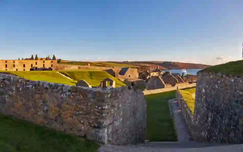 Stone walls and grassy ramparts of star-shaped Charles Fort overlook Kinsale Harbour under golden evening light.