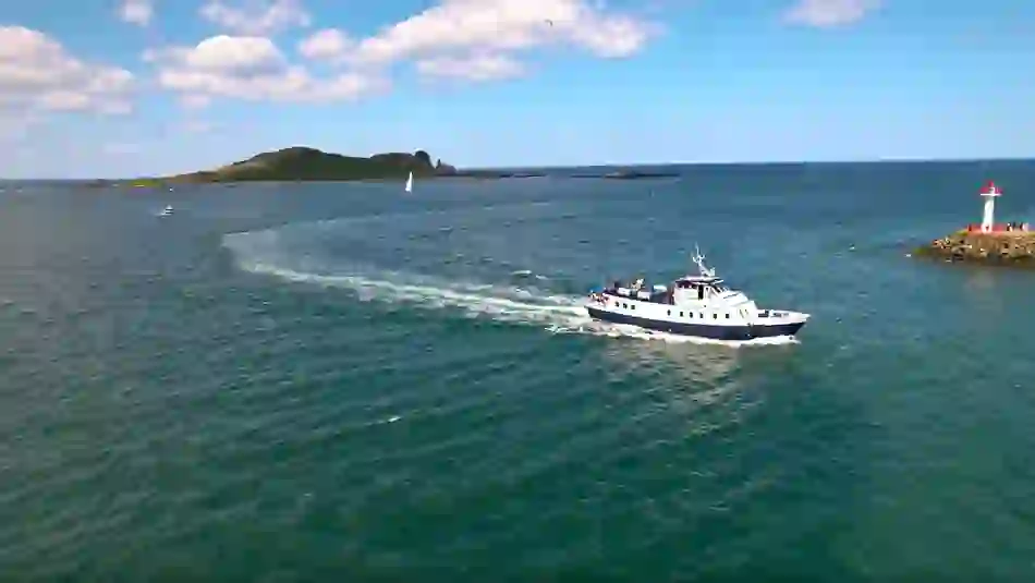 A sightseeing boat glides across the waters near a small lighthouse, with Ireland’s Eye in the distance.