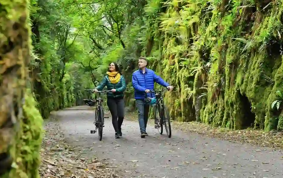 Two cyclists walking their bikes through a green, moss-lined path on the Waterford Greenway in County Waterford.