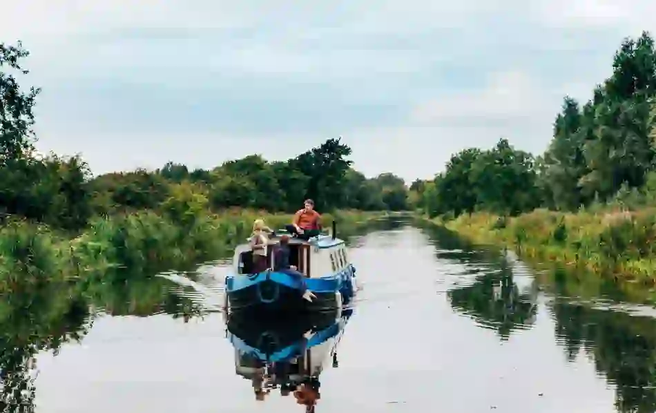 Family on a blue canal boat cruising through the Grand Canal in Sallins, County Kildare, surrounded by greenery.