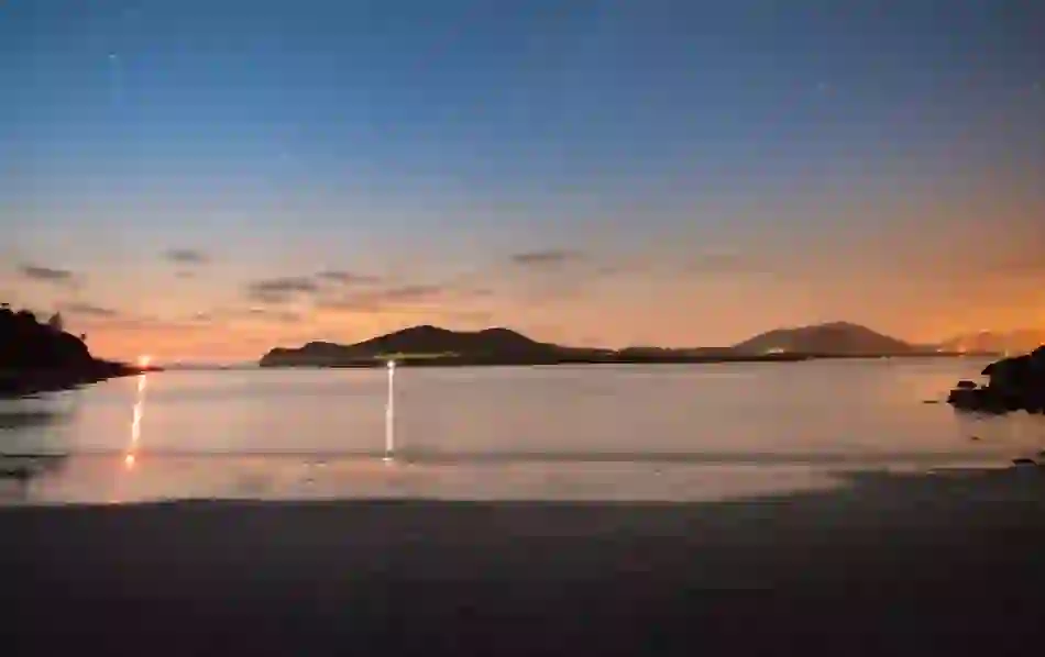 A tranquil night view over the Kerry International Dark Sky Reserve, with a star-filled sky reflecting on calm waters.