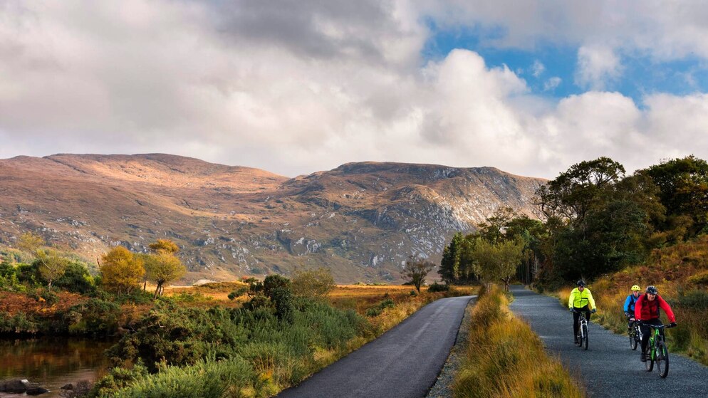 Scenic mountain road winds through Donegal’s northern headlands, with cyclists on a guided tour beneath a cloudy sky.