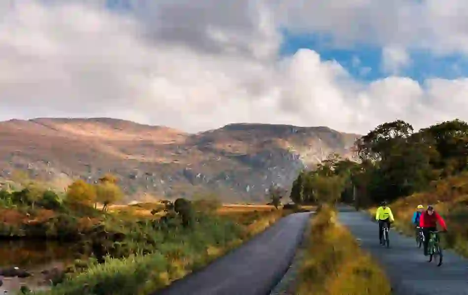 Scenic mountain road winds through Donegal’s northern headlands, with cyclists on a guided tour beneath a cloudy sky.